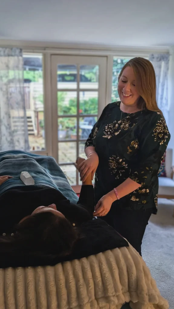 Kath Whitehorn performing a kinesiology session with a client lying comfortably on a treatment table at Hill Tribe Healing.