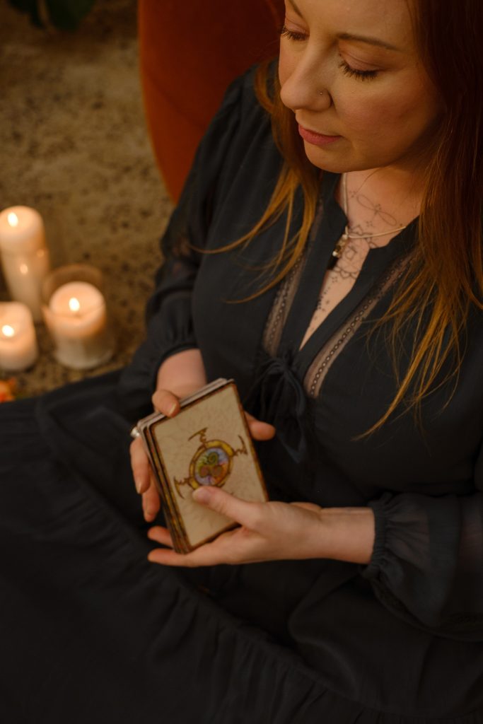 Kath Whitehorn holding a deck of cards beside candlelight in a calm, welcoming setting at Hill Tribe Healing.