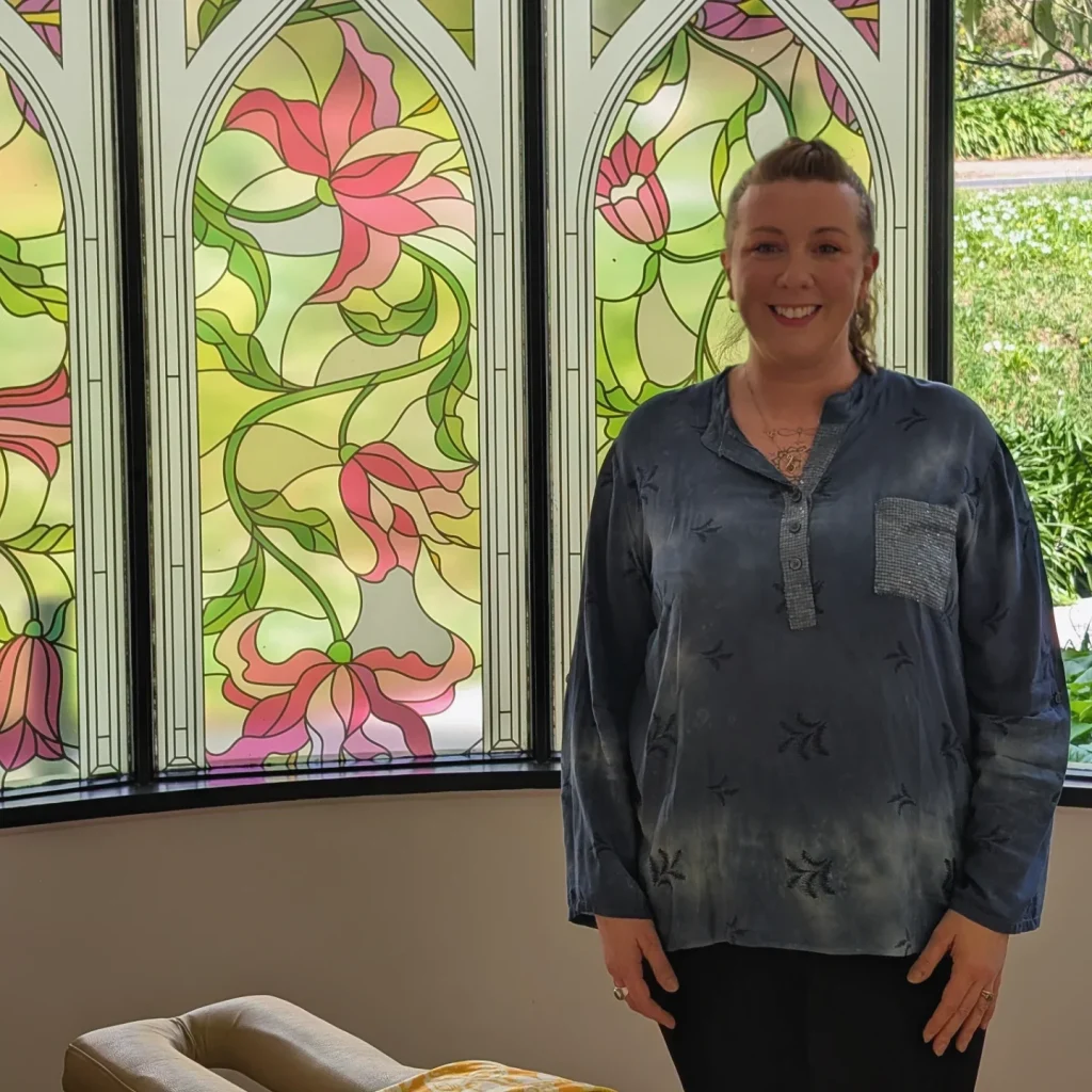 Kath Whitehorn standing inside the Soma Kallista treatment space, beside stained glass windows where Hill Tribe Healing sees clients on Saturdays.